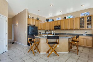 A modern kitchen with wooden cabinets, a central island with bar stools, a refrigerator, and a microwave.