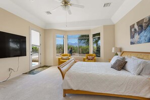 A bedroom with a bed, a television, a ceiling fan, and a large window with blinds.
