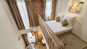 Een slaapkamer met een loft-stijl, met een bed met witte lakens en twee kussens, een bakstenen muur en een hanglamp.