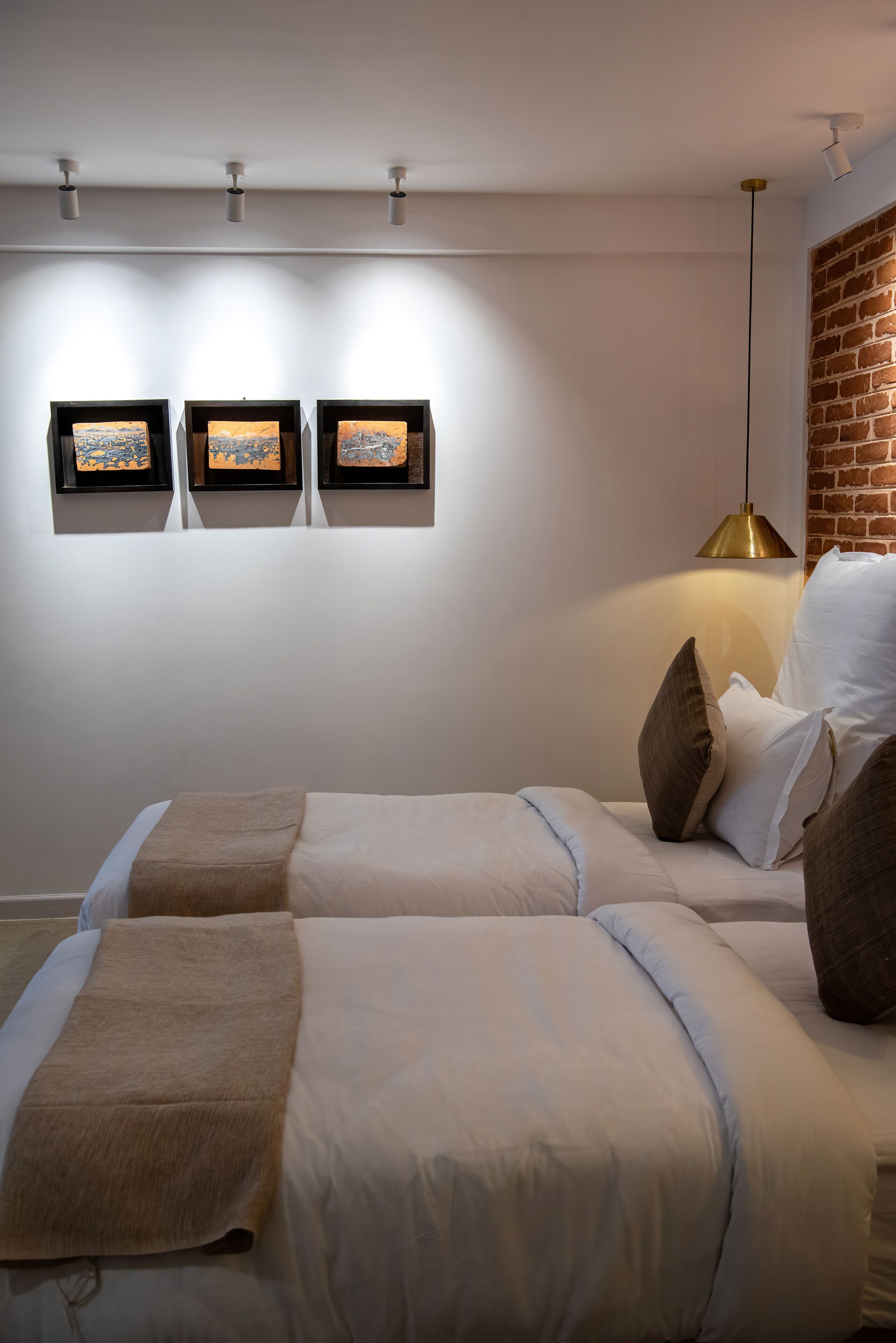 A hotel room with two beds, a brick wall, and three framed pictures on the wall.