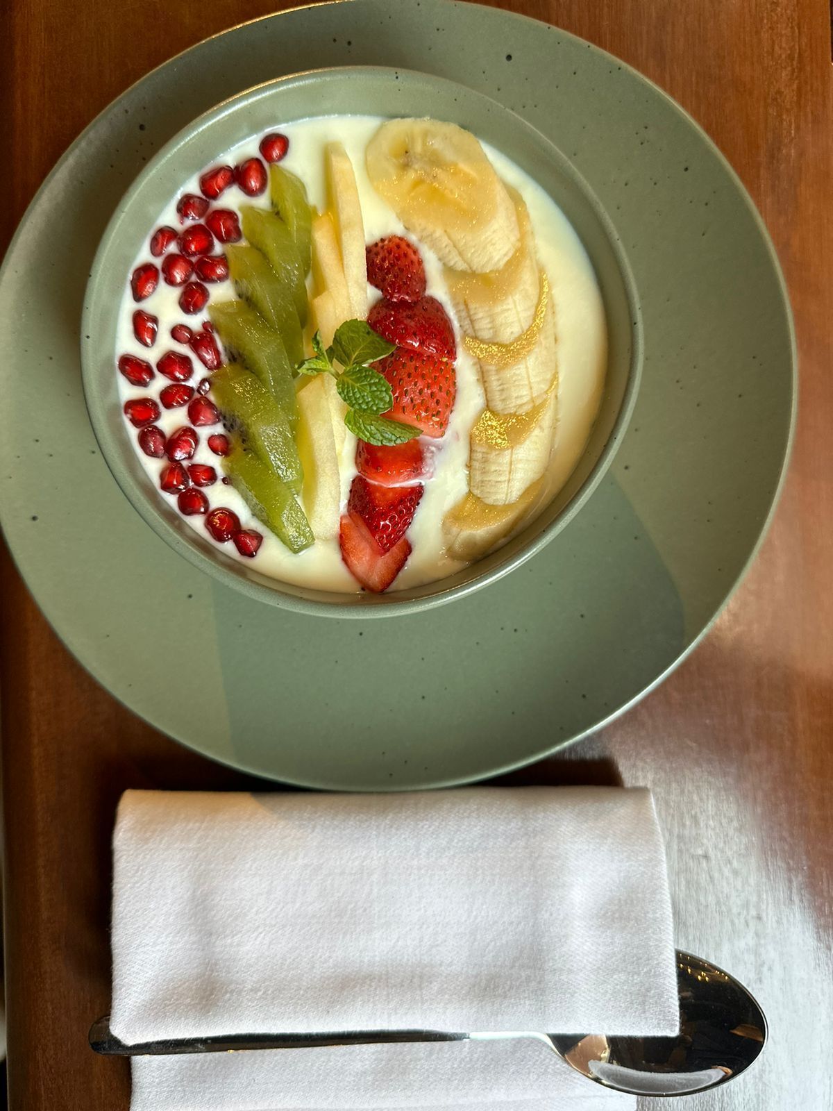 A bowl of yogurt topped with sliced bananas, strawberries, kiwi, and pomegranate seeds.