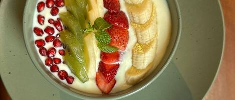 A bowl of yogurt topped with sliced bananas, strawberries, kiwi, and pomegranate seeds.