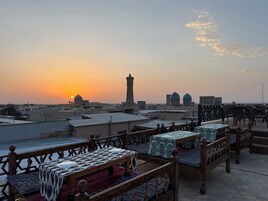 Terraza en la azotea con mesas y bancos, con vistas a un paisaje urbano con edificios con cúpulas y un minarete.