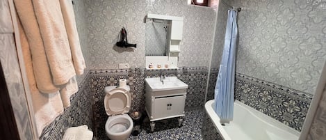 A bathroom with a toilet, sink, and bathtub, featuring patterned tiles and a hanging towel rack.