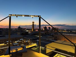 Una terraza en la azotea con mesas y sillas, vista al horizonte de la ciudad y un letrero que dice 'Suzangaron VIEW'.