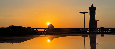 A sunset over a calm body of water with a prominent dome and a tall tower silhouetted against the sky.