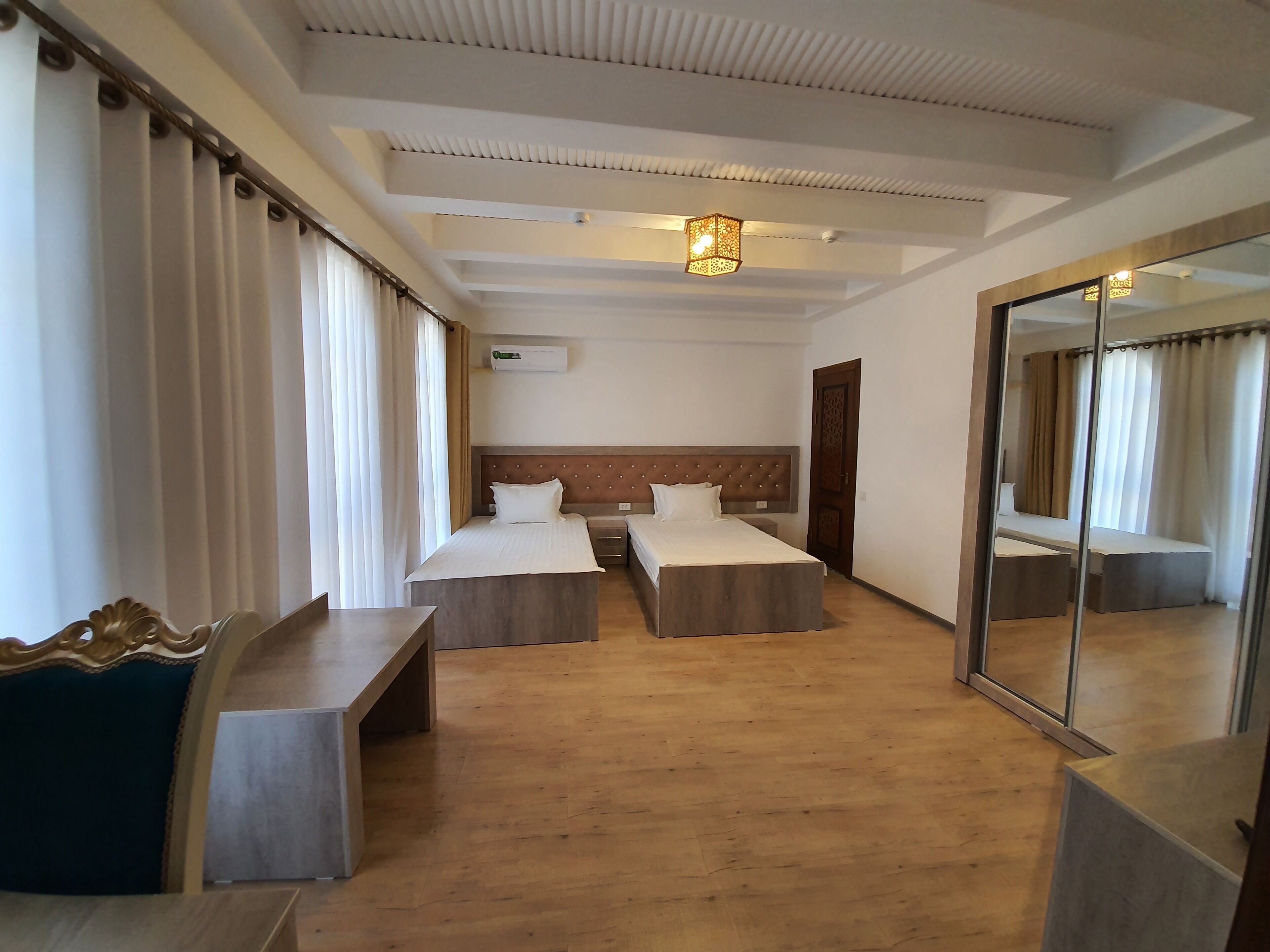 A hotel room with two single beds, a large mirror, a wooden floor, and a ceiling with recessed lighting.