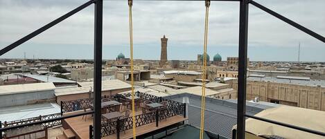 A wooden deck with a swing, overlooking a cityscape with historical buildings and a tower.