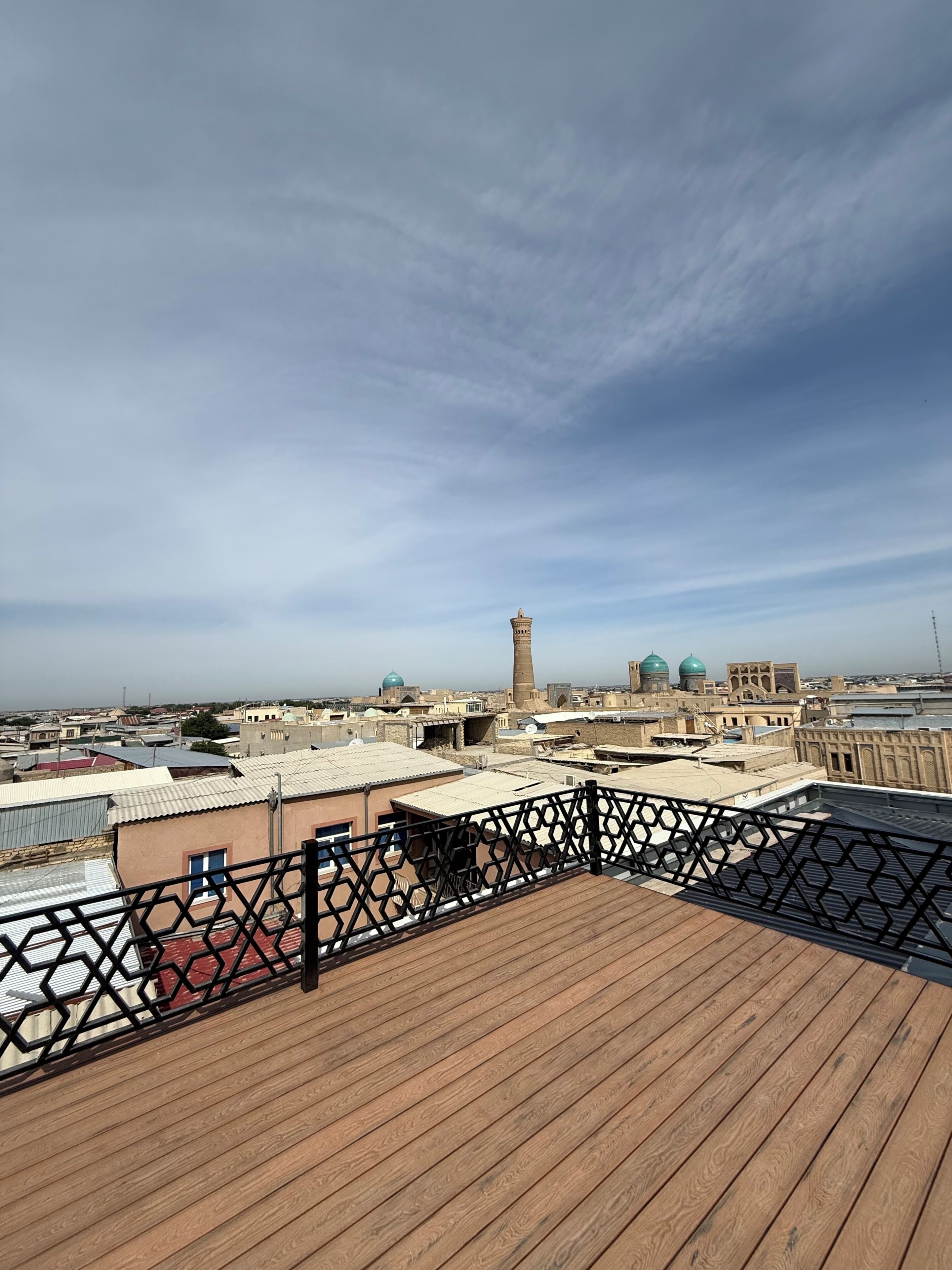 Un tetto con una terrazza in legno e ringhiera in metallo, affacciato su un panorama urbano con edifici e una torre.