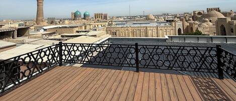 A wooden deck with a black railing overlooking a cityscape with historical architecture and a prominent tower.