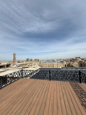 A wooden deck with a black railing overlooking a cityscape with historical architecture and a prominent tower.