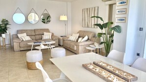 Un salon moderne avec un ensemble de canapés beige, une table basse blanche et une table à manger agrémentée d’un centre de table.