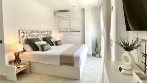 Une chambre à coucher moderne avec un lit, des tables de chevet, une télévision et un bureau agrémenté d’un vase.
