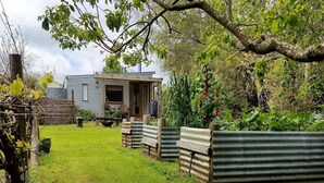 Un rustico chalet con veranda in legno e pareti in lamiera, circondato da vegetazione lussureggiante e un prato curato.