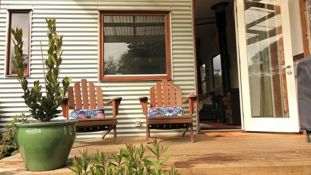 Un patio in legno con due poltrone Adirondack e un'ampia pianta in vaso.