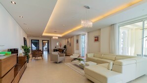 A spacious living area with a large beige sectional sofa, a wooden coffee table, and a dining area with a white table and chairs. - VB22 & VB23 by Qatar Coral (Doha)