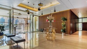 A modern lobby with a reflective floor, seating areas, a decorative table with a vase, and a city view through large windows. - VB22 & VB23 by Qatar Coral (Doha)