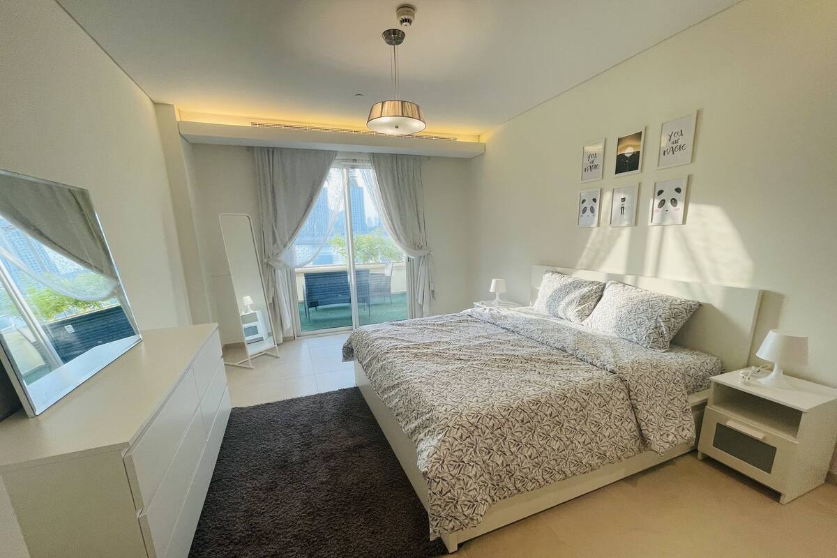 A modern bedroom with a large bed, a desk, and a view of a balcony.