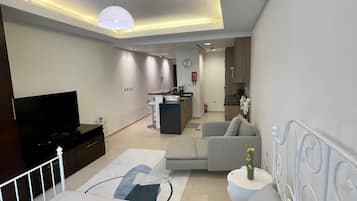 A modern bedroom with a bed, a TV, a sofa, and a small table with a vase.
