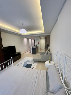 Un dormitorio moderno con cama, televisor, sofá y una mesita con un florero.