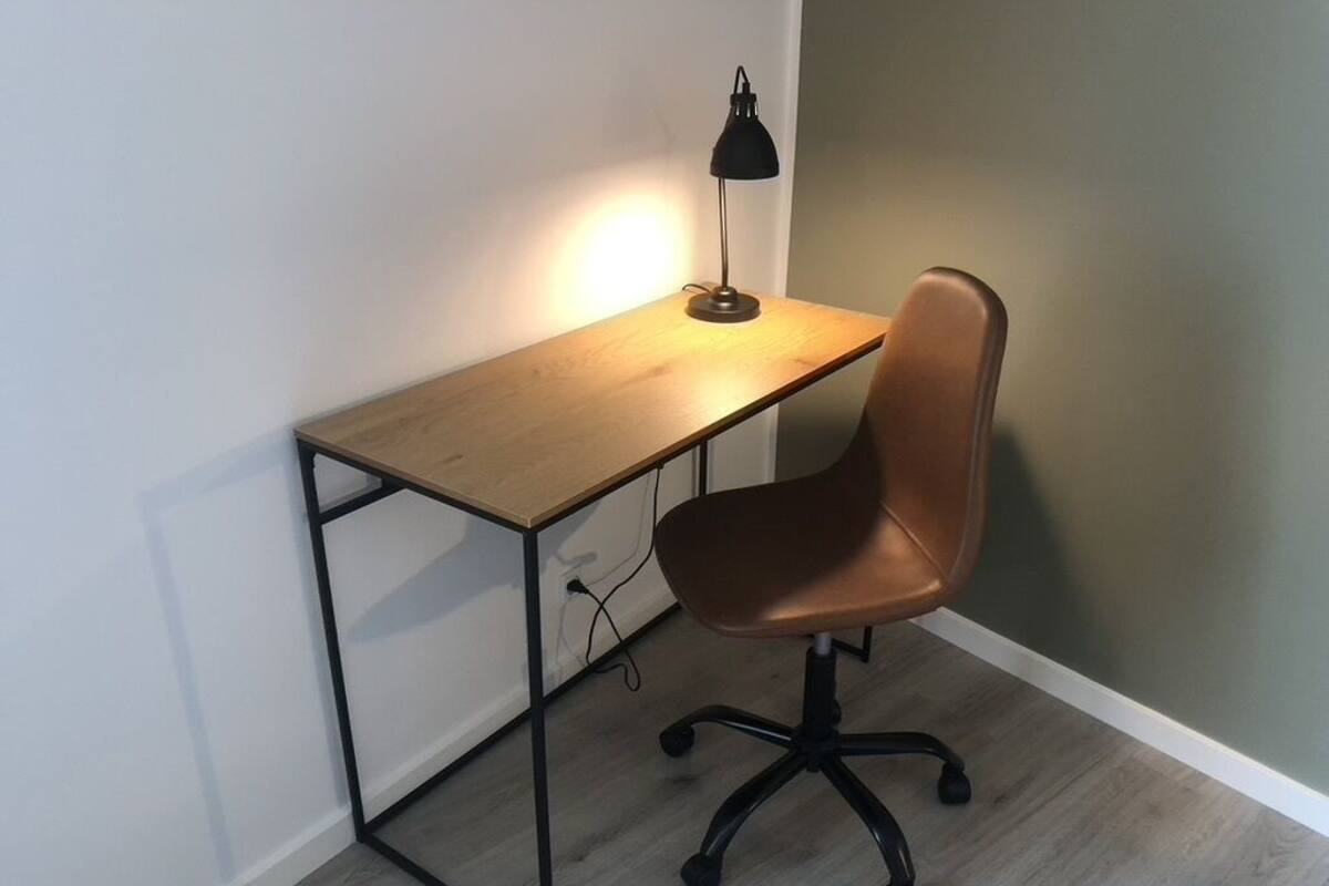 A desk with a lamp, a chair, and a wooden floor.