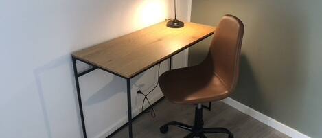 A desk with a lamp, a chair, and a wooden floor.