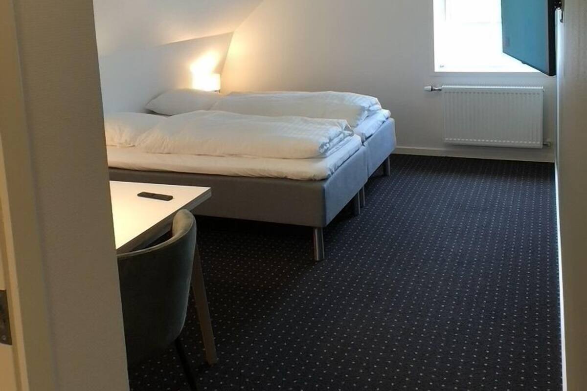 A small, modern room with a bed, a desk, and a window.