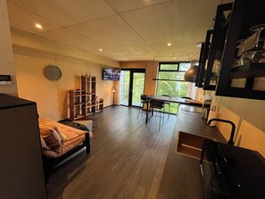 Ein modernes Wohnzimmer mit einer Couch, einem Essbereich mit Tisch und Stühlen, einem an der Wand befestigten Fernseher und einer Treppe zu einer oberen Ebene.