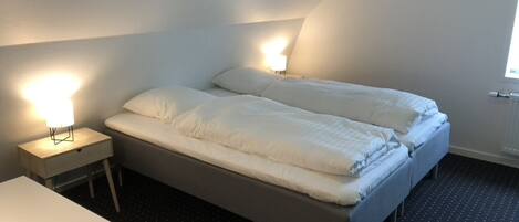 A small, dimly lit room with a single bed, a bedside table, and a nightstand.