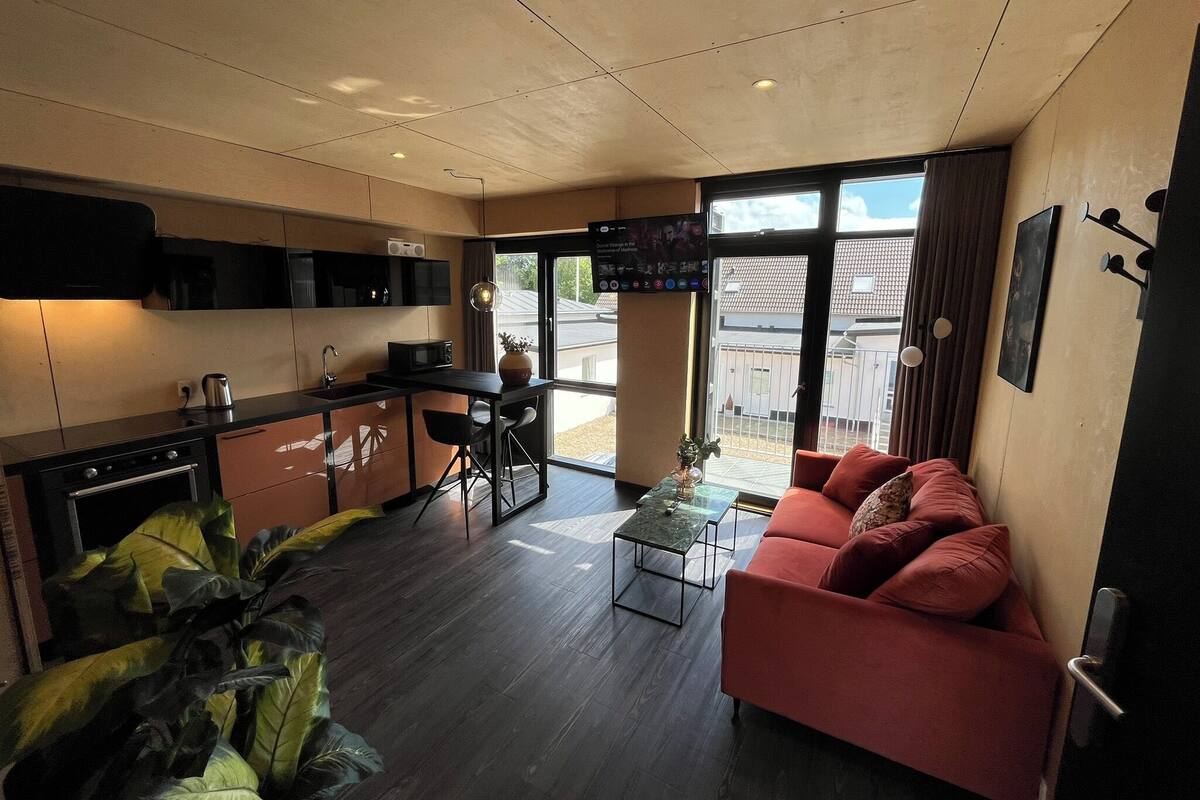 A modern kitchen with a dining area, a red sofa, and a large window with a view of the outside.