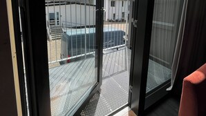 Een kamer met een schuifdeur die uitkomt op een buitenruimte met een metalen hek en een gebouw op de achtergrond.
