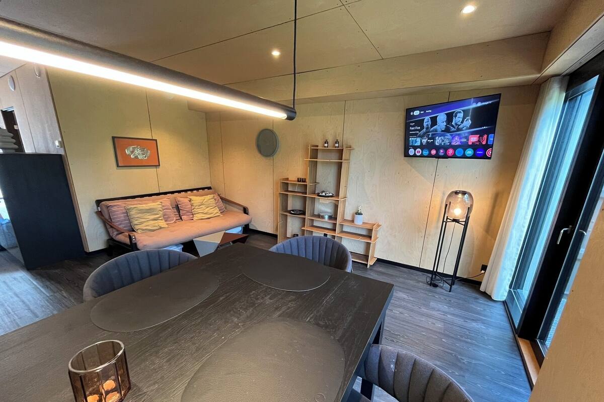 A modern living room with a large flat-screen TV mounted on the wall, a sofa, a coffee table, and a floor lamp.