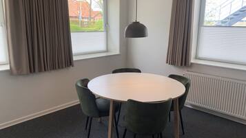 A modern dining area with a round table and four chairs, large windows with blinds, and a hanging pendant light.
