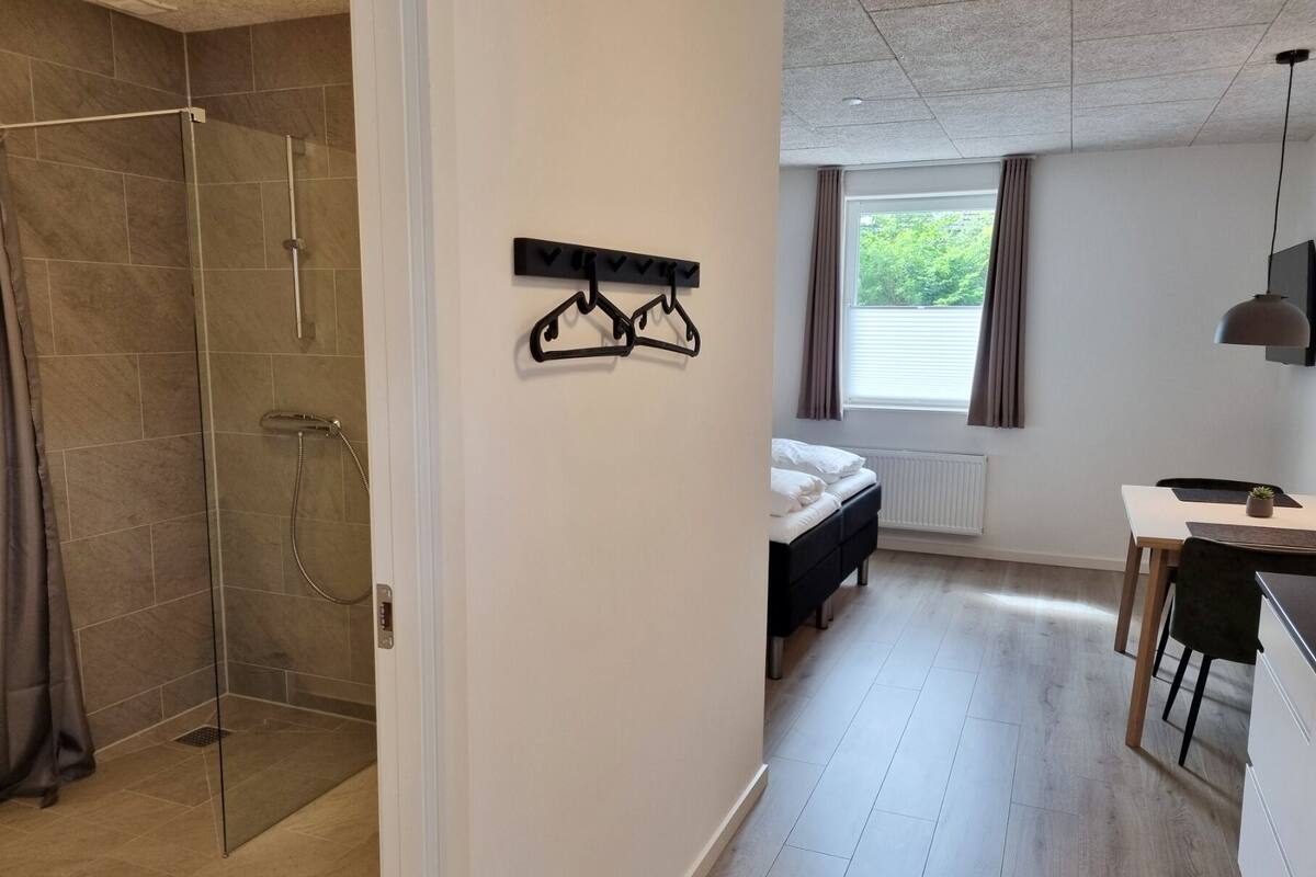 A modern hotel room with a shower, a bed, a desk, and a window with curtains.