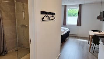 A modern hotel room with a shower, a bed, a desk, and a window with curtains.