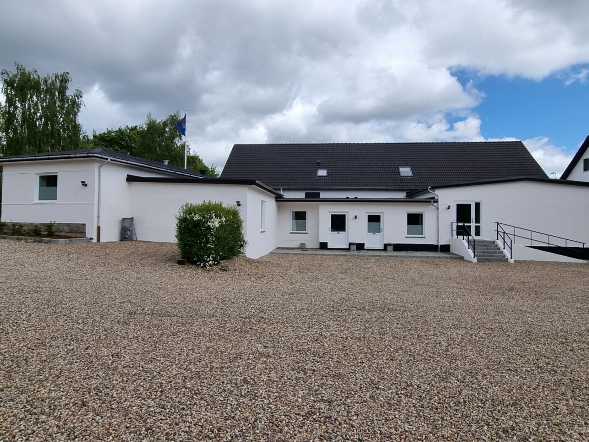 A modern building with a gravel driveway and a small bush.