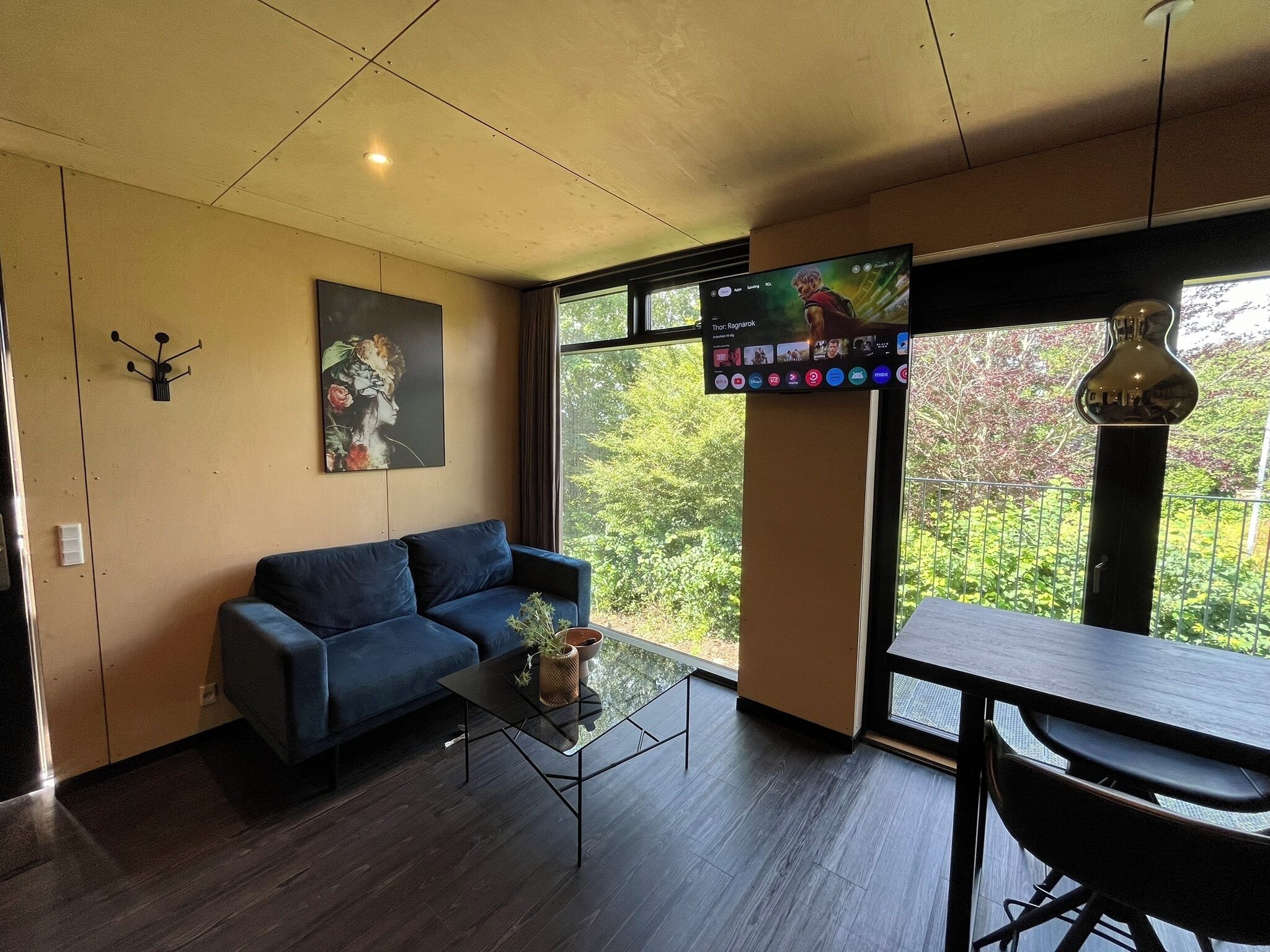 A modern living room with a blue sofa, a glass coffee table, and a TV mounted on the wall.