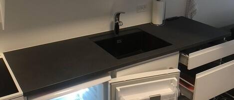 A kitchen with white cabinets, a black countertop, a sink, and a built-in refrigerator.
