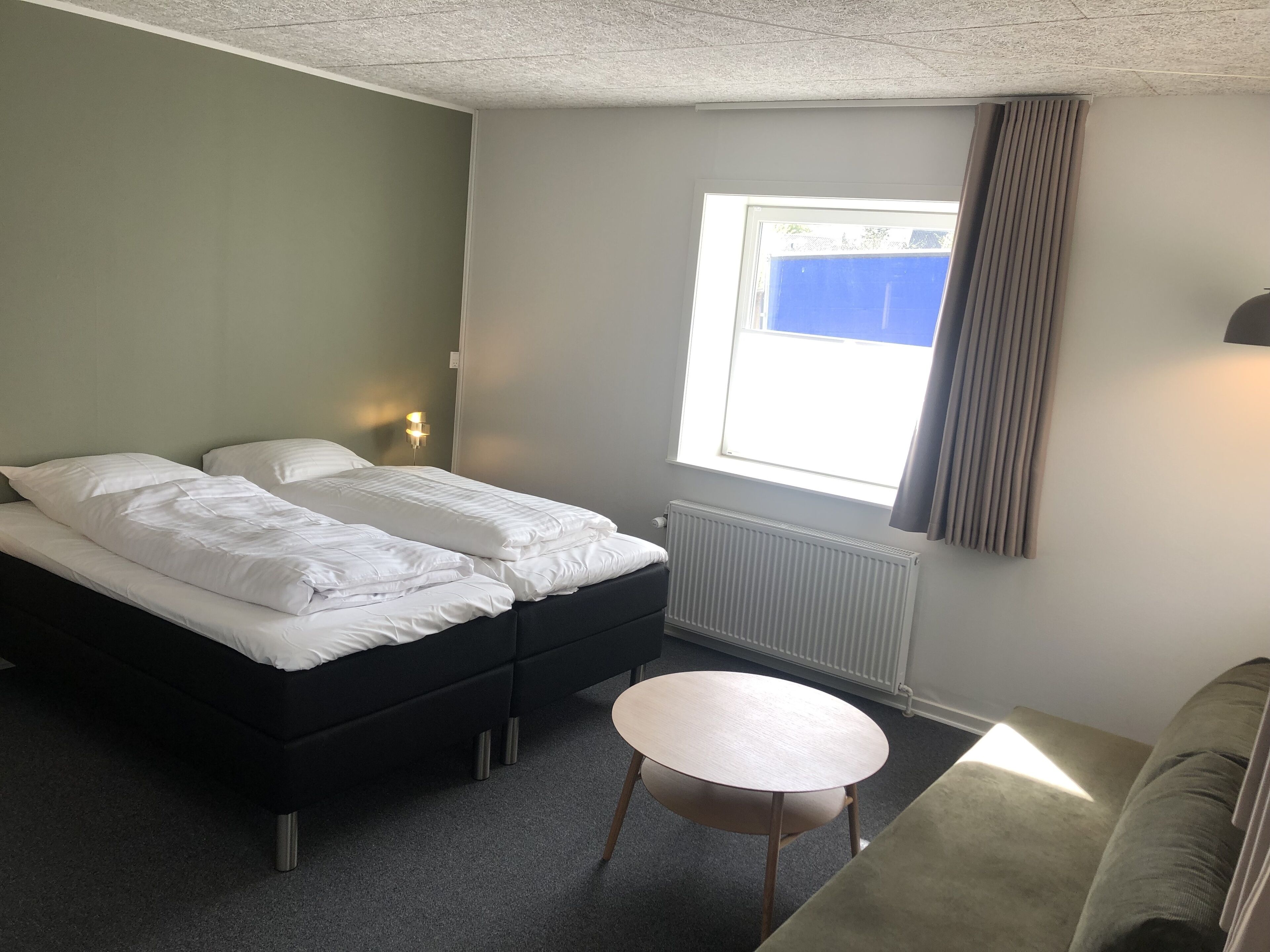 A room with two beds, a round table, a window with curtains, and a radiator.