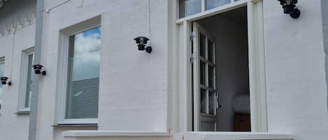 Um edifício com uma placa que diz "GO sleep" e uma janela com vista para o céu. Há degraus levando à entrada e duas plantas em vasos à frente.