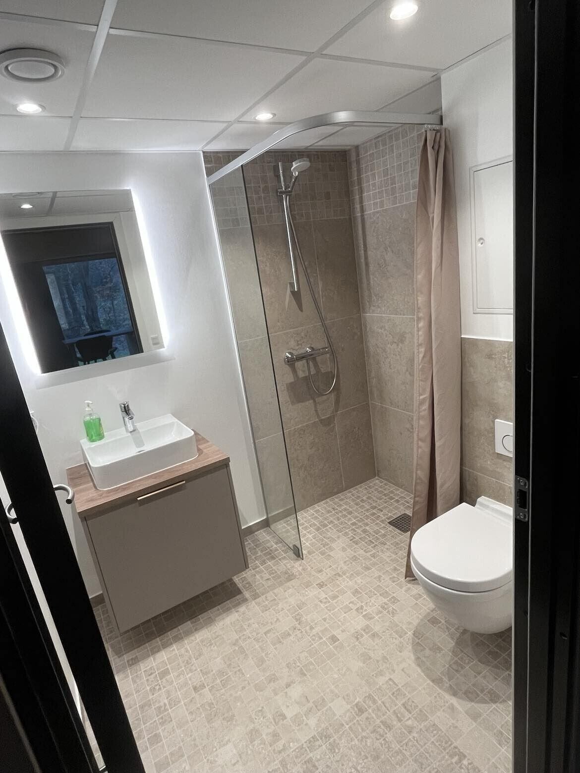 Un baño moderno con ducha envuelta en vidrio, un lavamanos con espejo y un inodoro.
