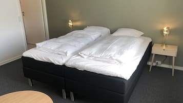 A double bed with white bedding, a small bedside table with a lamp, and a round wooden table.