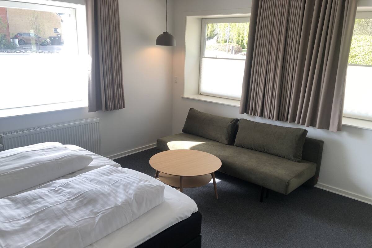 A hotel room with a bed, a sofa, a small round table, and a window with curtains.