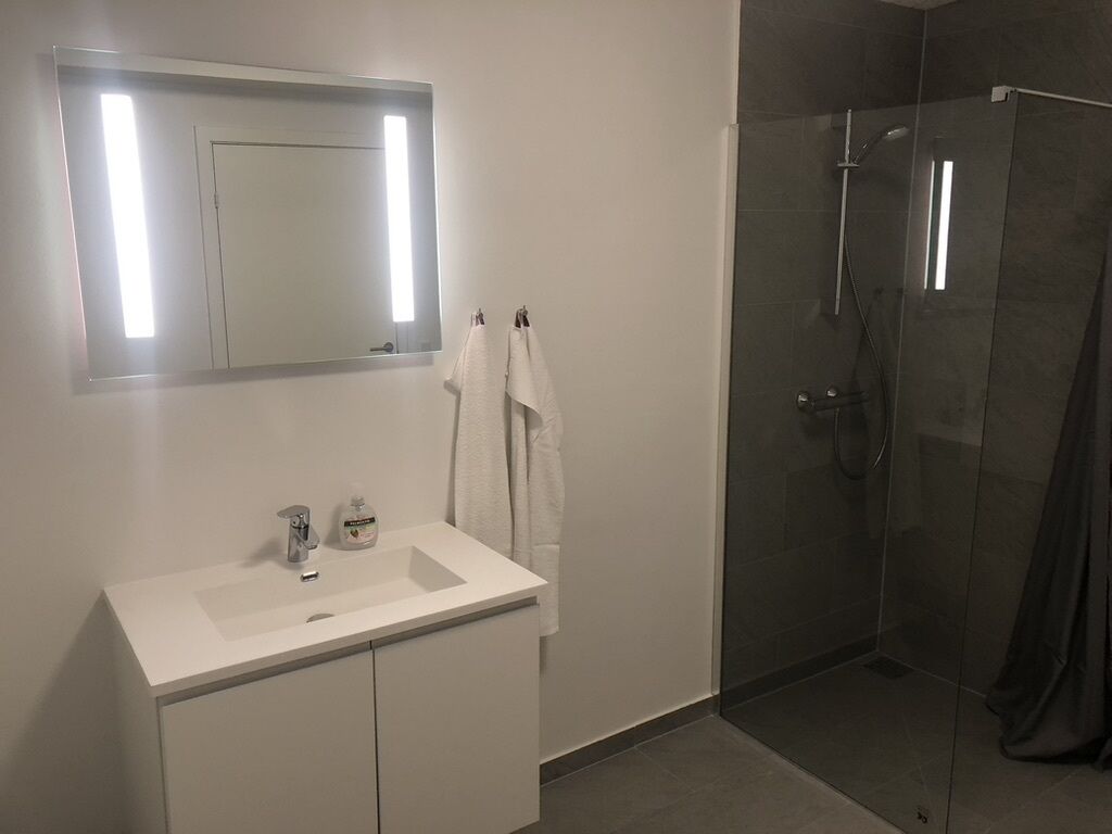 Un baño moderno con un tocador blanco, un espejo y una ducha con mampara de vidrio.