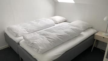 A single bed with white bedding in a room with a sloped ceiling and skylight.