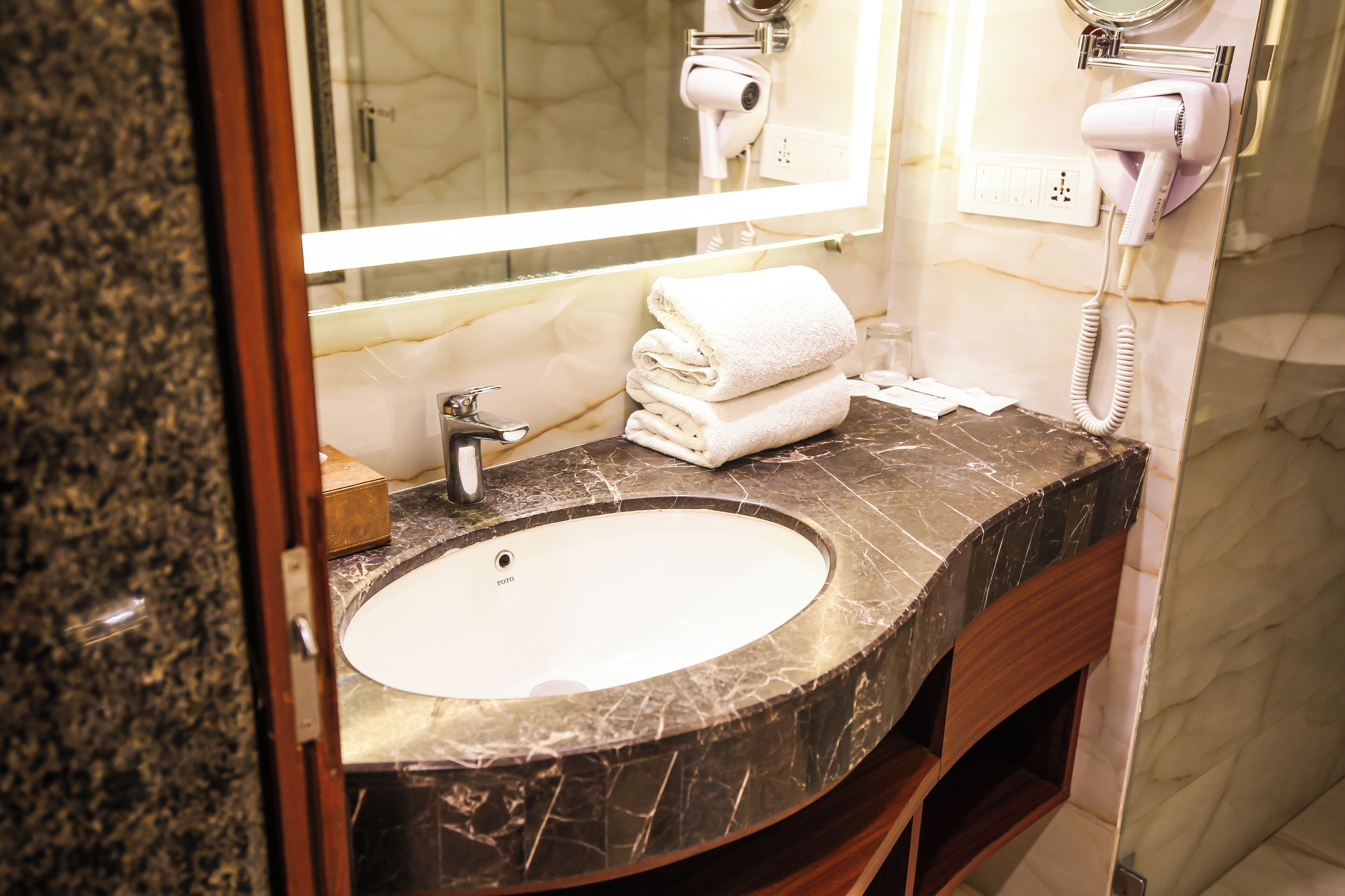 A bathroom with a marble sink, a mirror, a hairdryer, and a towel stack.
