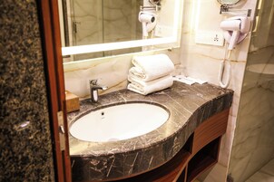 A bathroom with a marble sink, a mirror, a hairdryer, and a towel stack.