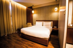 A hotel room with a large bed, wooden flooring, a headboard with a textured wall, two bedside tables, and a chair.