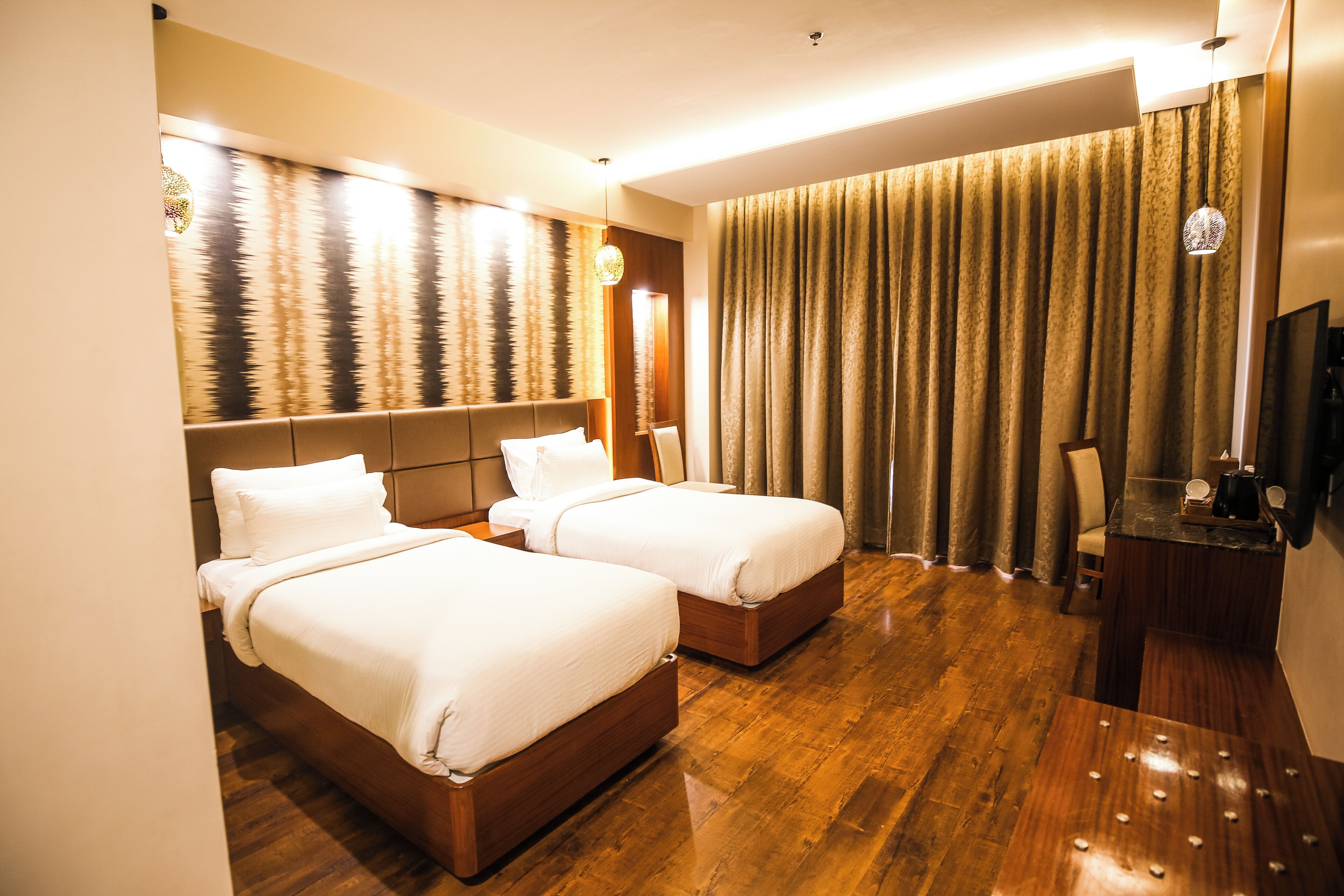 A hotel room with two beds, a desk, and a large window with curtains.