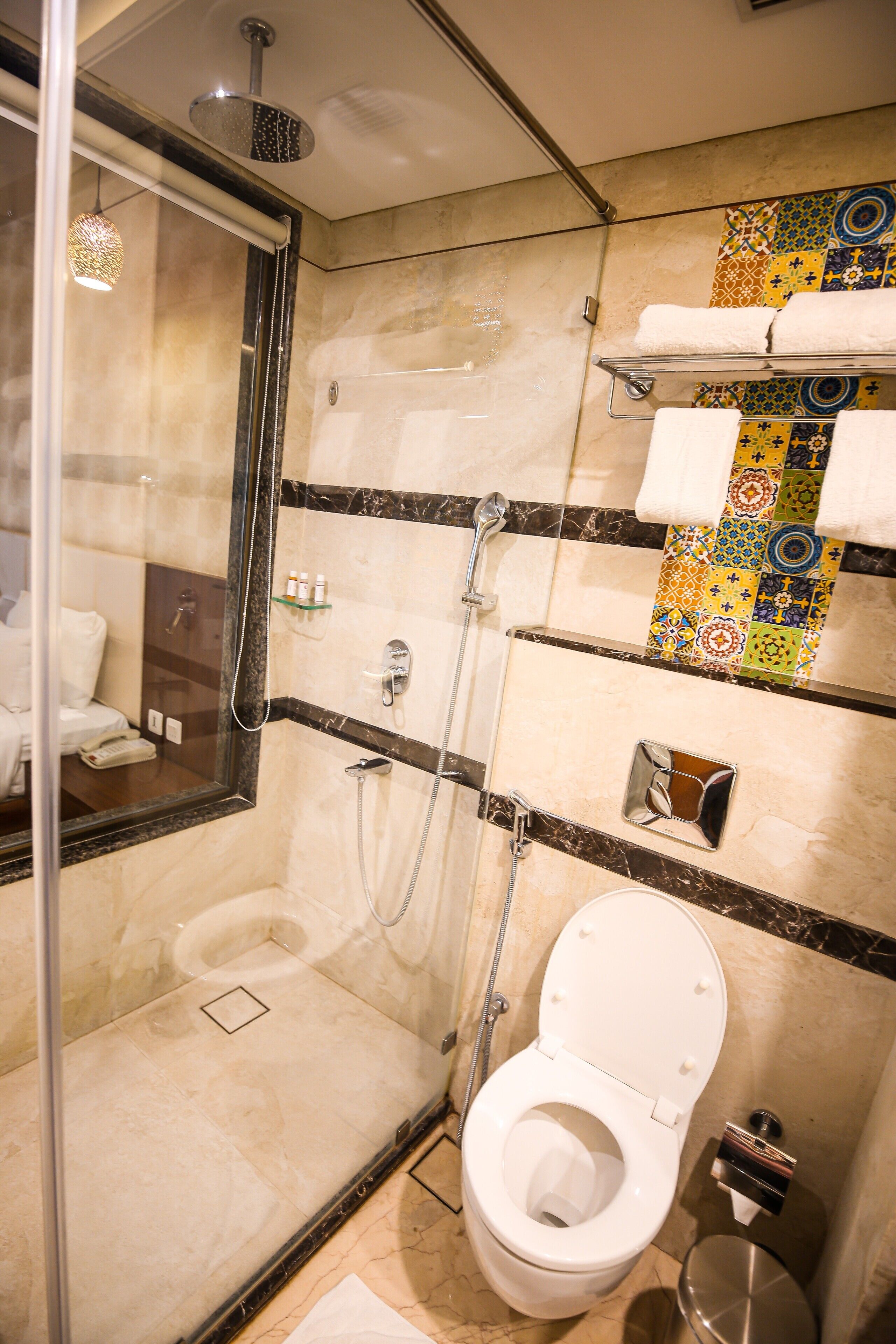 Un baño pequeño con ducha de mampara de vidrio, inodoro blanco y pared de azulejos con un estampado colorido.